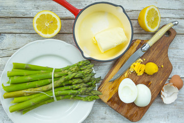 Green asparagus with ingredients for a yellow sauce on a wooden background. 