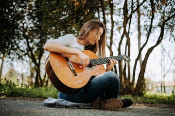 Young peaceful girl playing acoustic guitar in the park.
