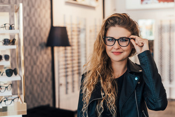 Pretty, young woman choosing new glasses frames in an optician store.