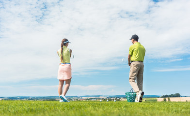 Full length of a young woman smiling while practicing the correct move for striking during golf class with a skilled professional player outdoors