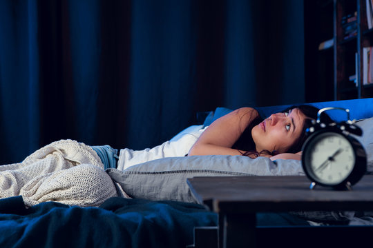 Image of dissatisfied woman with insomnia lying on bed next to alarm clock at night