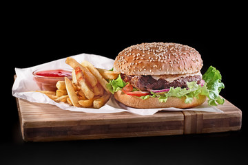 burger with french fries on wooden cutting board isolated on black background