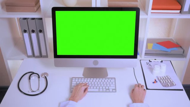 top view on the desk with stethoscope medical prescription and pills in white bottle. unrecognizable doctor wearing in white lab coat sitting in front of the computer with green screen typing on