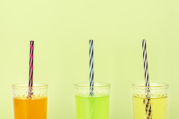 Transparent glass glasses with straws and orange, lime and pear lemonade on green background. The...
