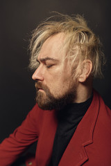 Side view. Perfect to the last detail. Handsome young blond man in studio with dark background. Punk rock theater