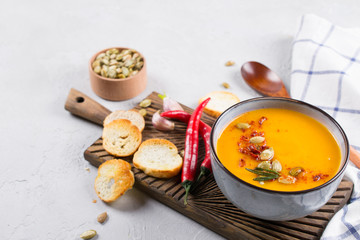 Vegetable cream soup with seeds, toast and seasoning in a ceramic bowl on a table.