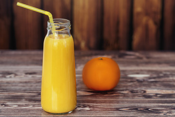 bottle with orange juice and orange on wooden wall background.