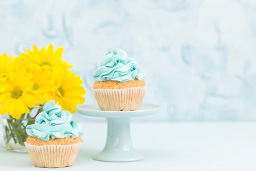 Cupcake with yellow cream decoration on vintage stand and bouquet of yellow chrysanthemum in glasses vase.