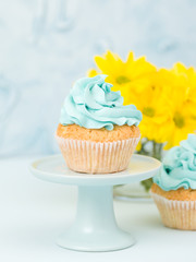 Cupcake with blue cream decoration on vintage stand and bouquet of yellow chrysanthemum in glasses vase.