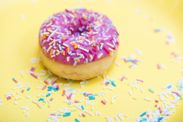 Pink Donut with sprinkles on yellow background 