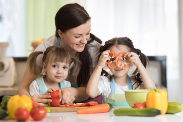 Happy family mom and kids preparing vegetables together at home in the kitchen