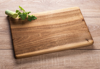 Wooden kitchen cutting Board on wooden background with greenery.