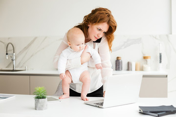 Portrait of business woman standing with her little baby in hand and talking on her cellphone while working on  laptop isolated