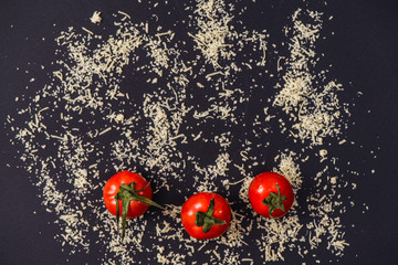 grated parmesan cheese and tomatoes on black background