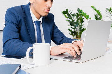African american businessman typing on laptop keyboard by office table