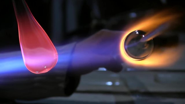 A glass crafter is burning and blowing an art piece. Glassblowing Professional Working on Torch Flame with Glass Tubes. Glass blower forming beautiful piece of glass