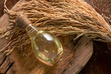 Bottle of rice bran oil and unmilled rice on wooden background