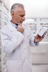 Be attentive. Mature thoughtful male pharmacist touching chin while holding medication