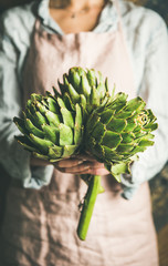 Female farmer wearing pastel linen apron and shirt holding fresh artichokes in her hands, selective...