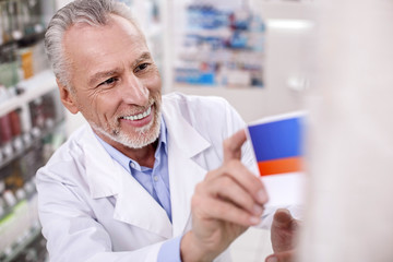 Pharmaceutical industry. Senior exuberant male pharmacist placing drug on shelf while grinning