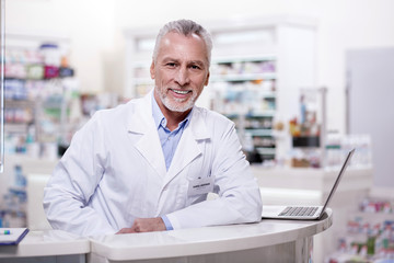 Ready for work. Senior exuberant male pharmacist staring at camera while leaning on stand