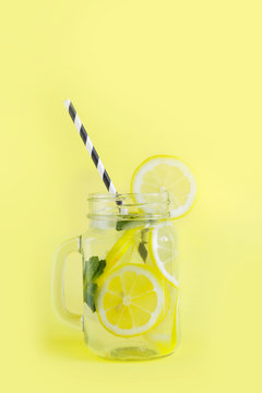 Summer refreshing cocktail with lemon, mint and ice in mason jar on yellow. Tropical concept.