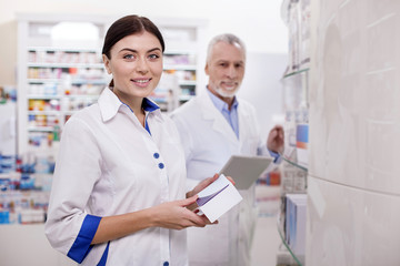 Responsible obligations. Optimistic female pharmacist smiling to camera while holding drug