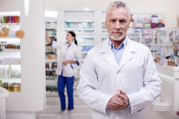 Naklejka na ściany i meble Calm confidence. Mature successful male pharmacist standing on blurred background while looking at camera