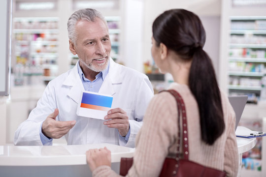 Best choice. Mature handsome male pharmacist holding drug while chatting with client