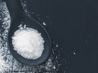 Obraz na płótnie Canvas White salt in spoon on black background