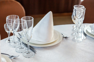 Glasses, flowers, fork, knife, napkin folded in a pyramid, served for dinner in restaurant with cozy interior. Wedding decorations and items for food, arranged by the catering service on a large table