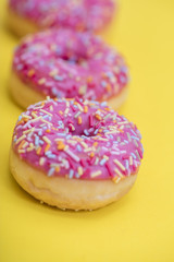Sprinkled Pink Donut. Frosted sprinkled donut on yellow background.