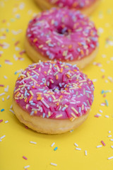 Pink Donut with sprinkles on yellow background 