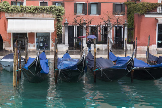 Parked covered gandolas on a pier in front of the old Venice shops.