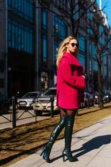 Fashion vogue style young beautiful stylish woman walking in pink coat, sunglasses, shorts and high heel jackboots. Happy, street city style, spring trend, white shirt, sexy. Tourism Saint-Petersburg