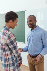 African american teacher talking to high school student in classroom