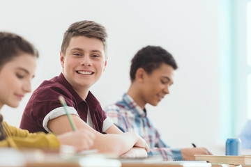 Smiling caucasian schoolboy sitting at desk between classmates