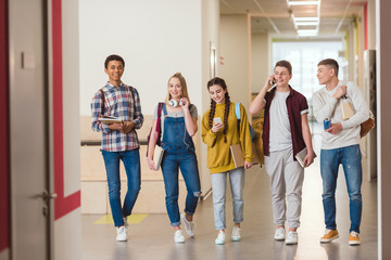 happy high school classmates walking by school corridor together