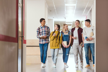 group of smiling high school classmates walking by school corridor together