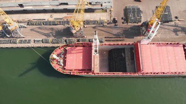 Aerial view of the ship's loading near the berth in the cargo port during the day. Loading of wire rod into ship's hold by ship cranes. Video from the drone 4K.