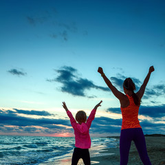 healthy mother and daughter on seacoast on sunset rejoicing