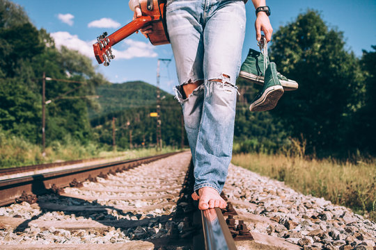 Young man with guitar walks on railway road, close up legs image