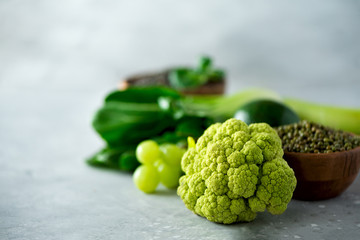 Organic green vegetables and fruits on grey background. Copy space, flat lay, top view. Green apple, zucchini, cucumber, avocado, kale, lime, kiwi, grapes, banana, broccoli, marbled lentils, mung bean