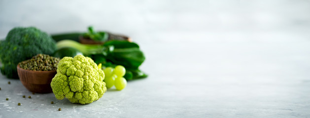 Organic green vegetables and fruits on grey background. Copy space, flat lay, top view. Green apple, avocado, kale, lime, kiwi, grapes, broccoli, marbled lentils, mung bean. Banner