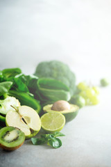 Green smoothie in glass jar with fresh organic green vegetables and fruits on grey background. Spring diet, healthy raw vegetarian, vegan concept, detox breakfast, alkaline clean eating. Copy space