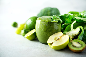 Fototapeta na wymiar Glass with green health smoothie, kale leaves, lime, apple, kiwi, grapes, banana, avocado, lettuce. Copy space. Raw, vegan, vegetarian, alkaline food concept.