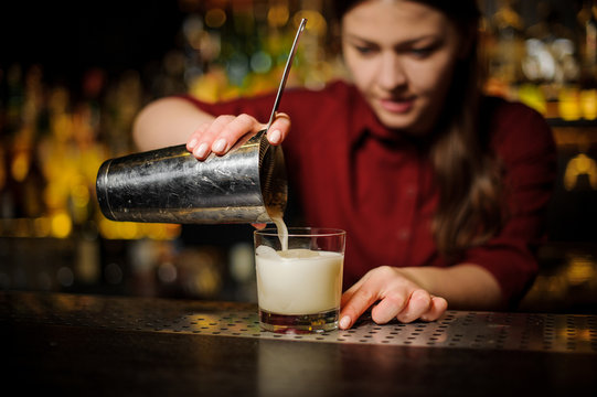 Female bartender pouring out a white cocktail from the shaker
