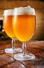 Two glasses of cold beer standing on wooden table