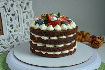 Delicious rustic naked homemade cake decorated with cream, chocolate, mint and berries.