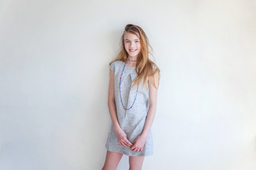 Happy teenage girl smiling. Closeup portrait young happy positive woman in grey dress at home in bright room against white wall. European woman. Positive human emotion facial expression body language